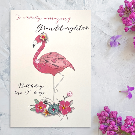Front Image of white card with pink flamingo, surrounded with flowers, sequins and script text
