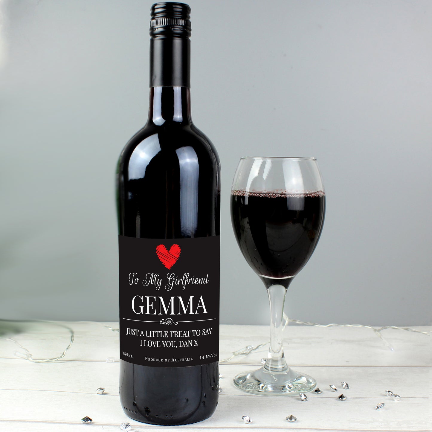 Wine bottle with a personalized label next to a glass of red wine on a light wooden surface.