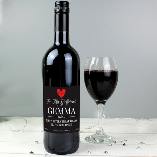 Wine bottle with a personalized label next to a glass of red wine on a light wooden surface.