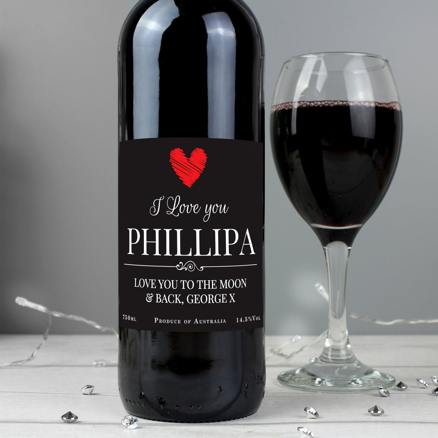 Wine bottle with personalized label next to a glass of red wine on a gray background