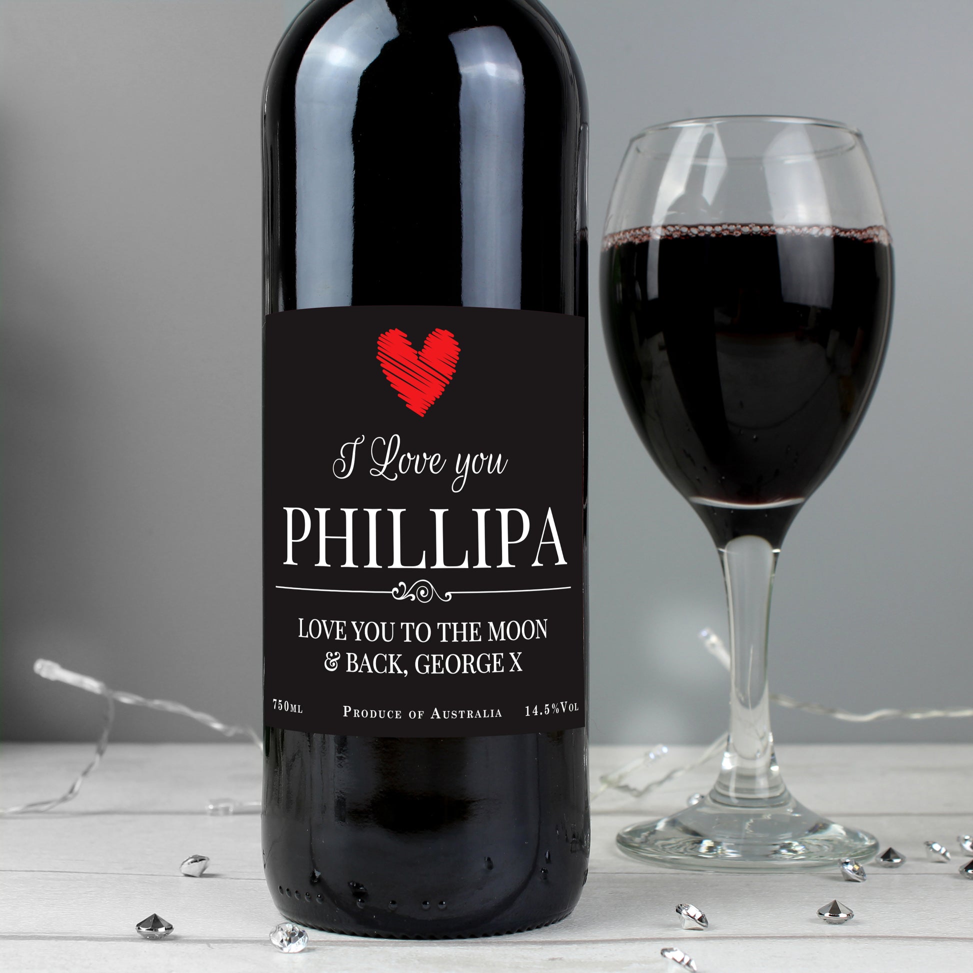 Wine bottle with personalized label next to a glass of red wine on a gray background