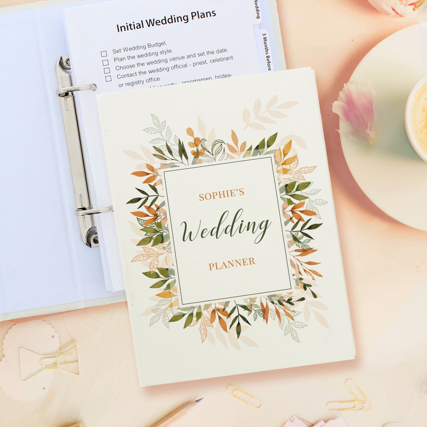 Wedding planner book with floral design and 'Sophie's Wedding Planner' text, placed on a surface with stationery items.