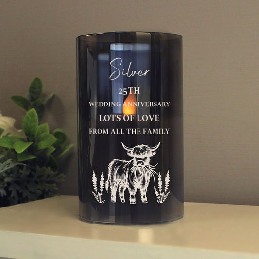 Black candle with white personalised text and a cow illustration on a table with a plant in the background