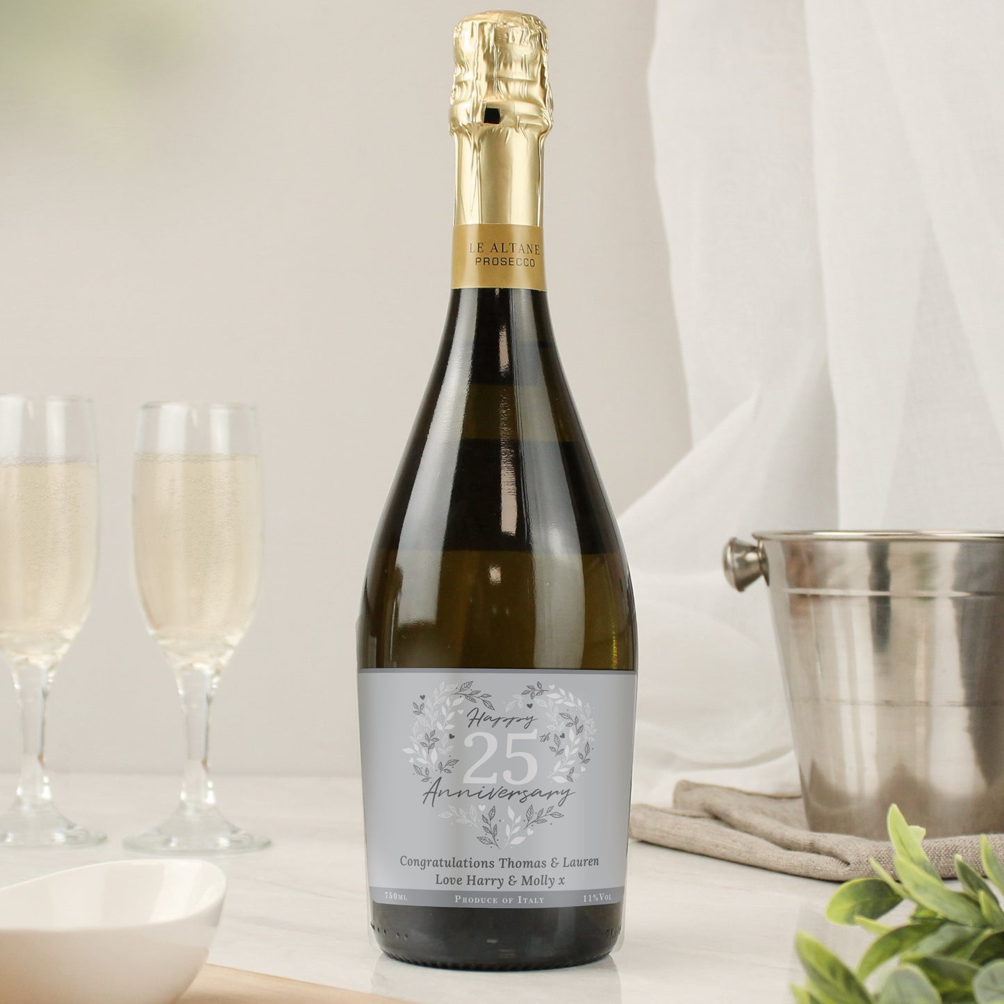 Dark green bottle of prosecco with happy anniversary label shown on a surface with wine bucket and flutes
