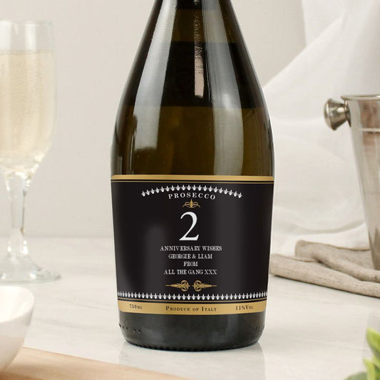 Bottle of Prosecco with a personalized label on a table with glasses.