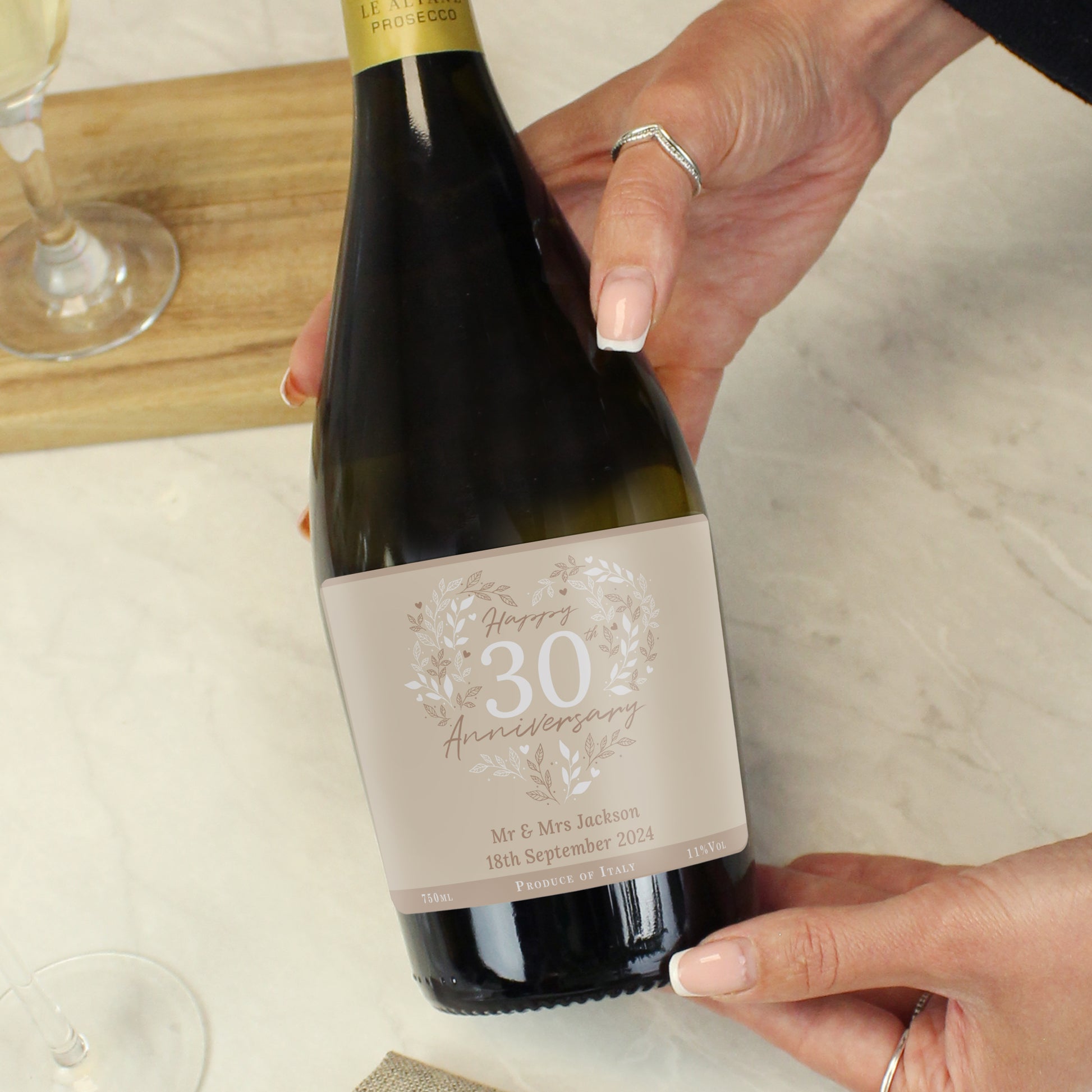 Person holding a wine bottle with a personalised label, set against a neutral background.