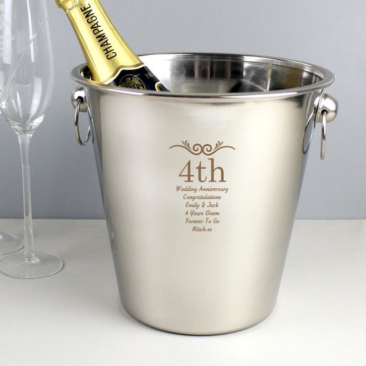 Stainless steel ice bucket with engraved text and a bottle of champagne on a white surface.