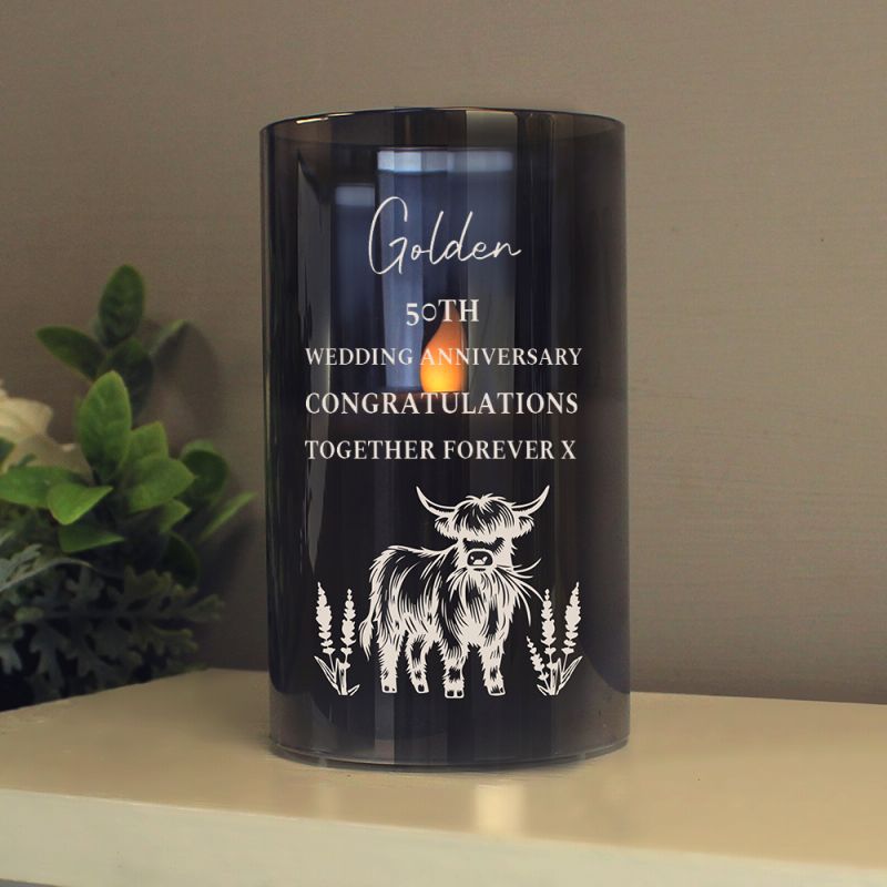 Black candle with white personalised text and cow illustration on a table with a plant in the background