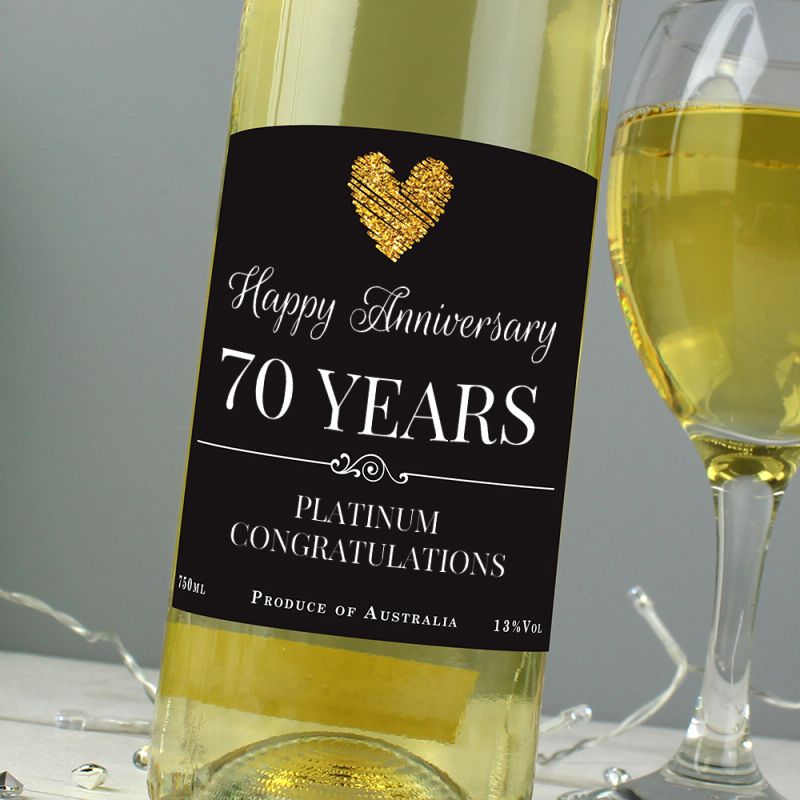 Bottle of white wine with a 'Happy Anniversary 65 Years' label next to a glass of wine on a grey background.