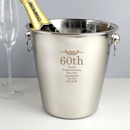 Stainless steel ice bucket with engraved text and a bottle of champagne on a white surface.