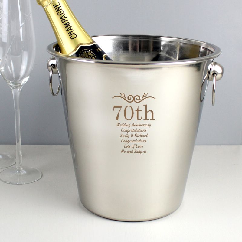 Stainless steel ice bucket with engraved text and a bottle of champagne on a white surface.