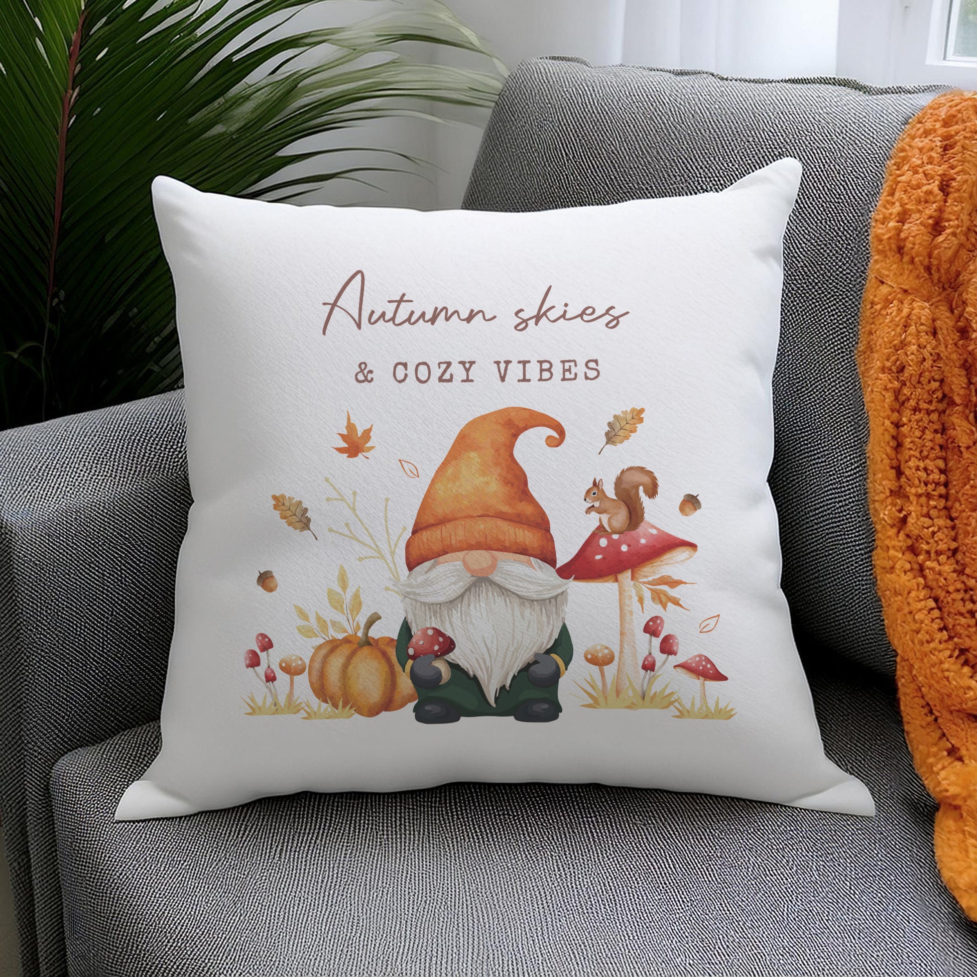 Decorative personalised pillow with autumn-themed design featuring a gnome, pumpkins, and leaves on a grey couch.
