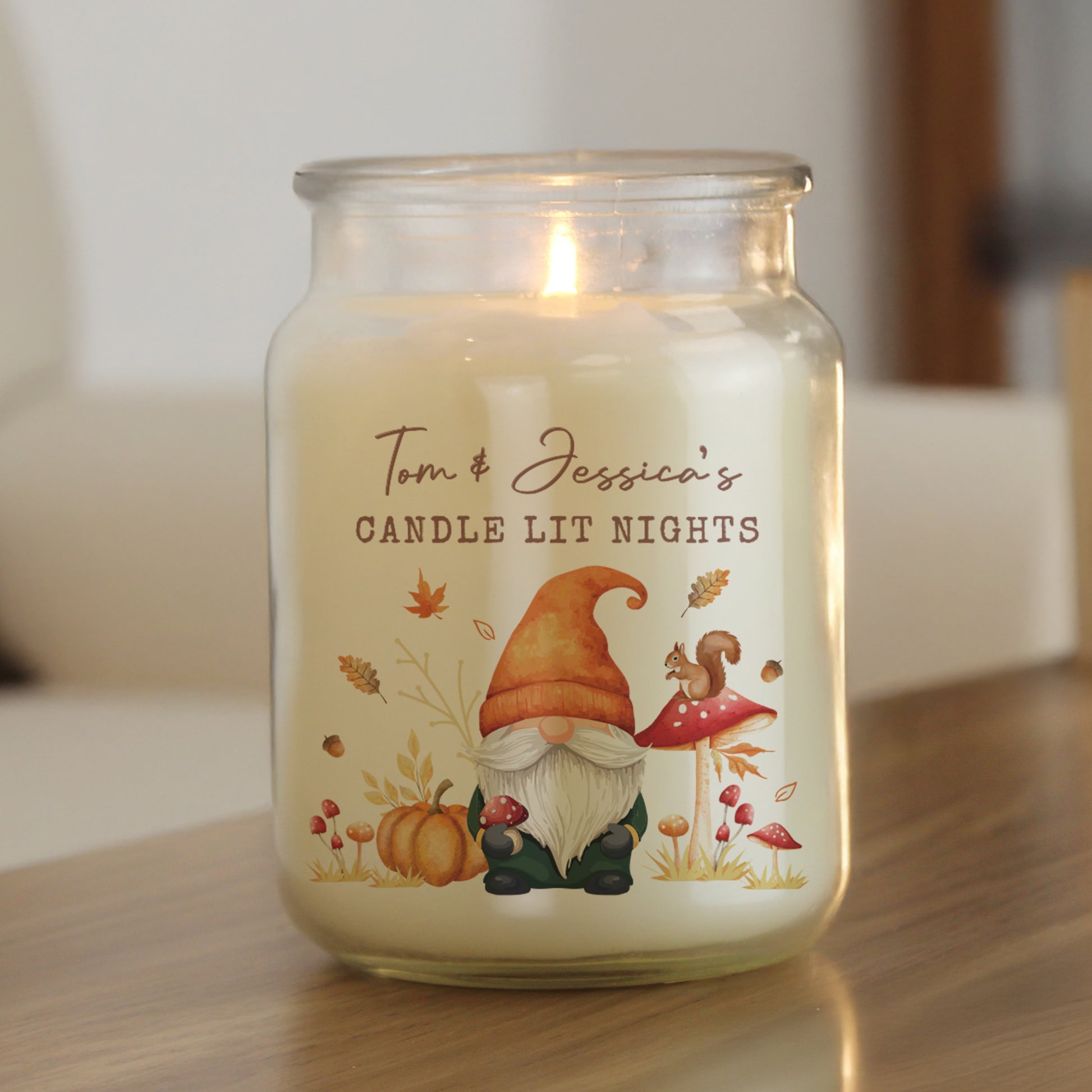 Candle in a glass jar with a personalised label featuring a gnome, mushroom, and pumpkin design on a wooden surface.