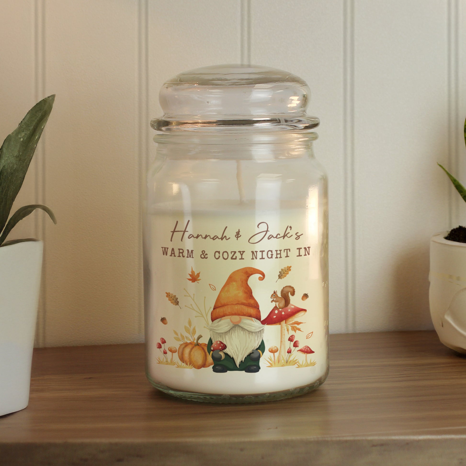 Decorative personalised candle jar with a gnome design and text on a wooden surface.