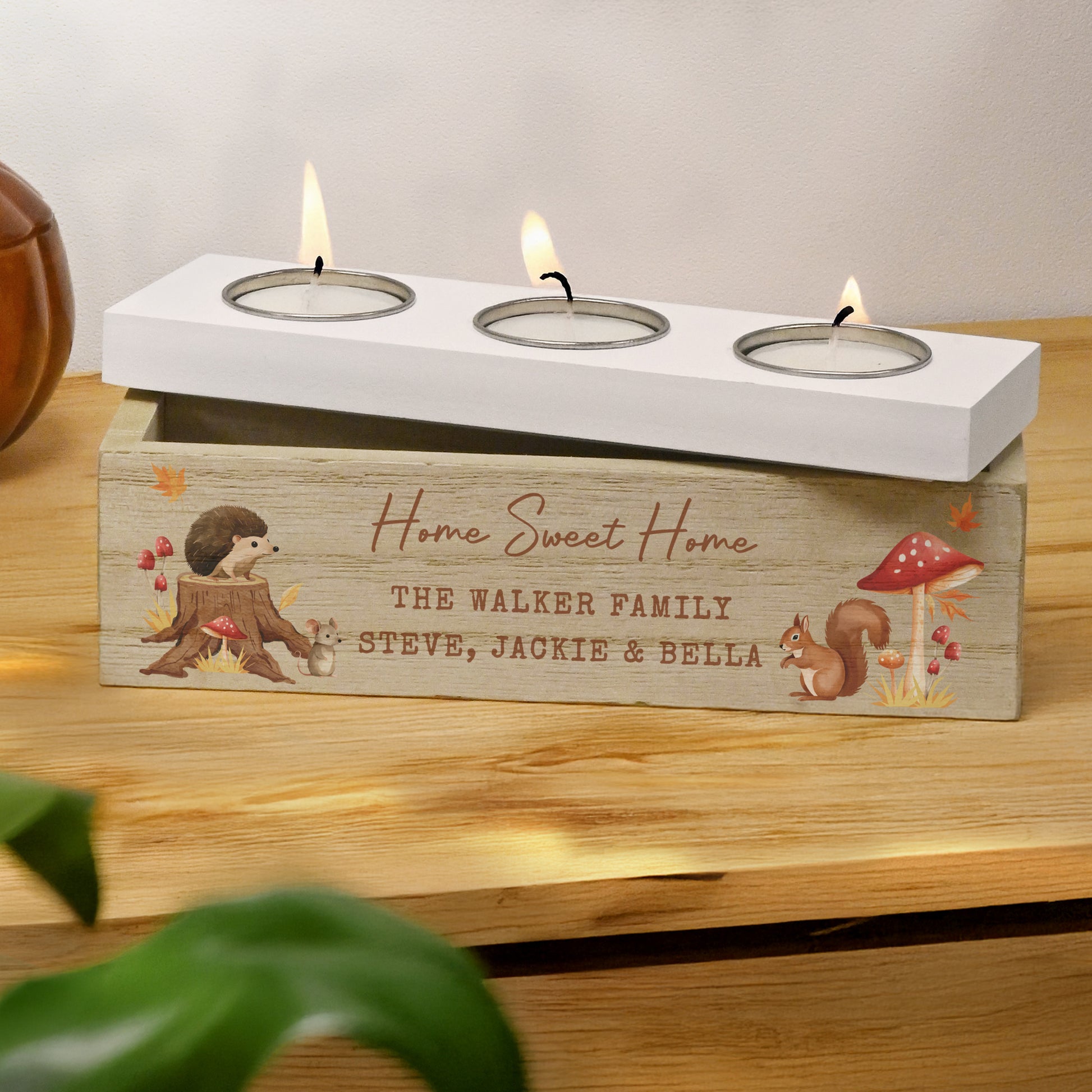 Wooden candle holder with 'Home Sweet Home' engraving and three lit candles on a wooden surface.