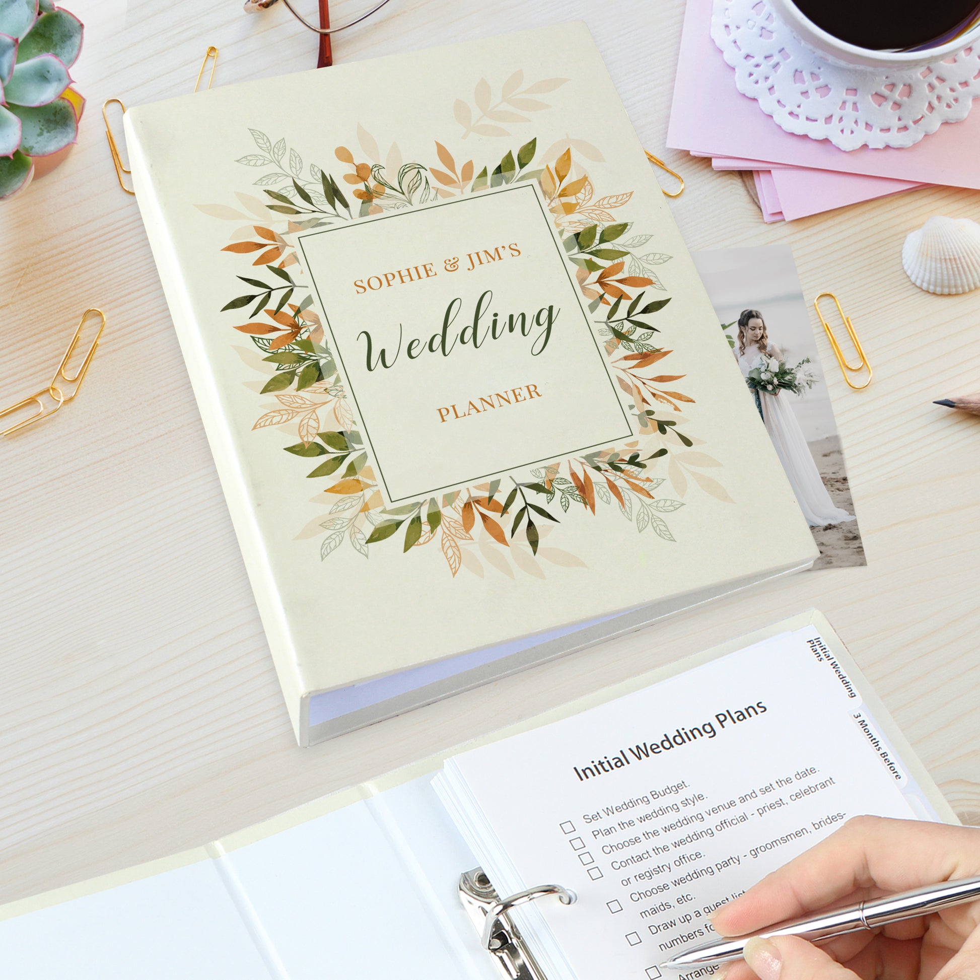 Wedding planner book with floral design on a desk with a cup of coffee and stationery.