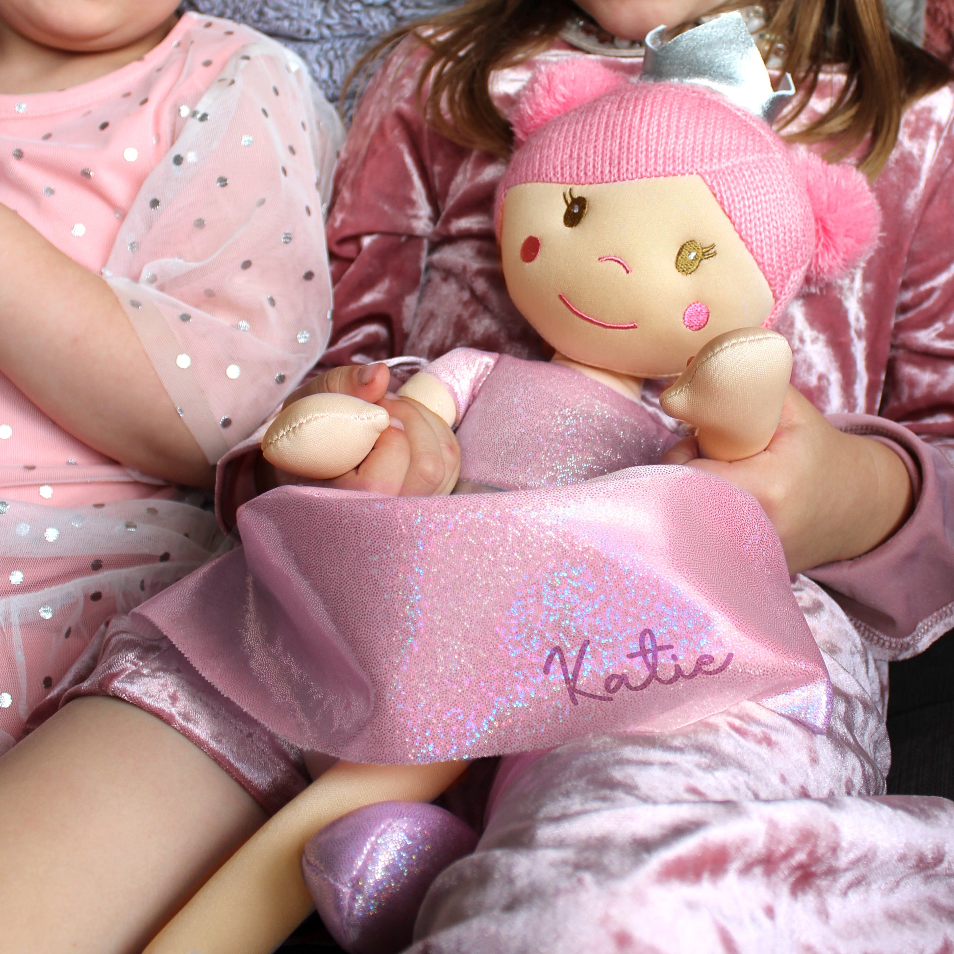 Child holding a plush toy with 'Natalie' embroidered on it, wearing pink outfit.