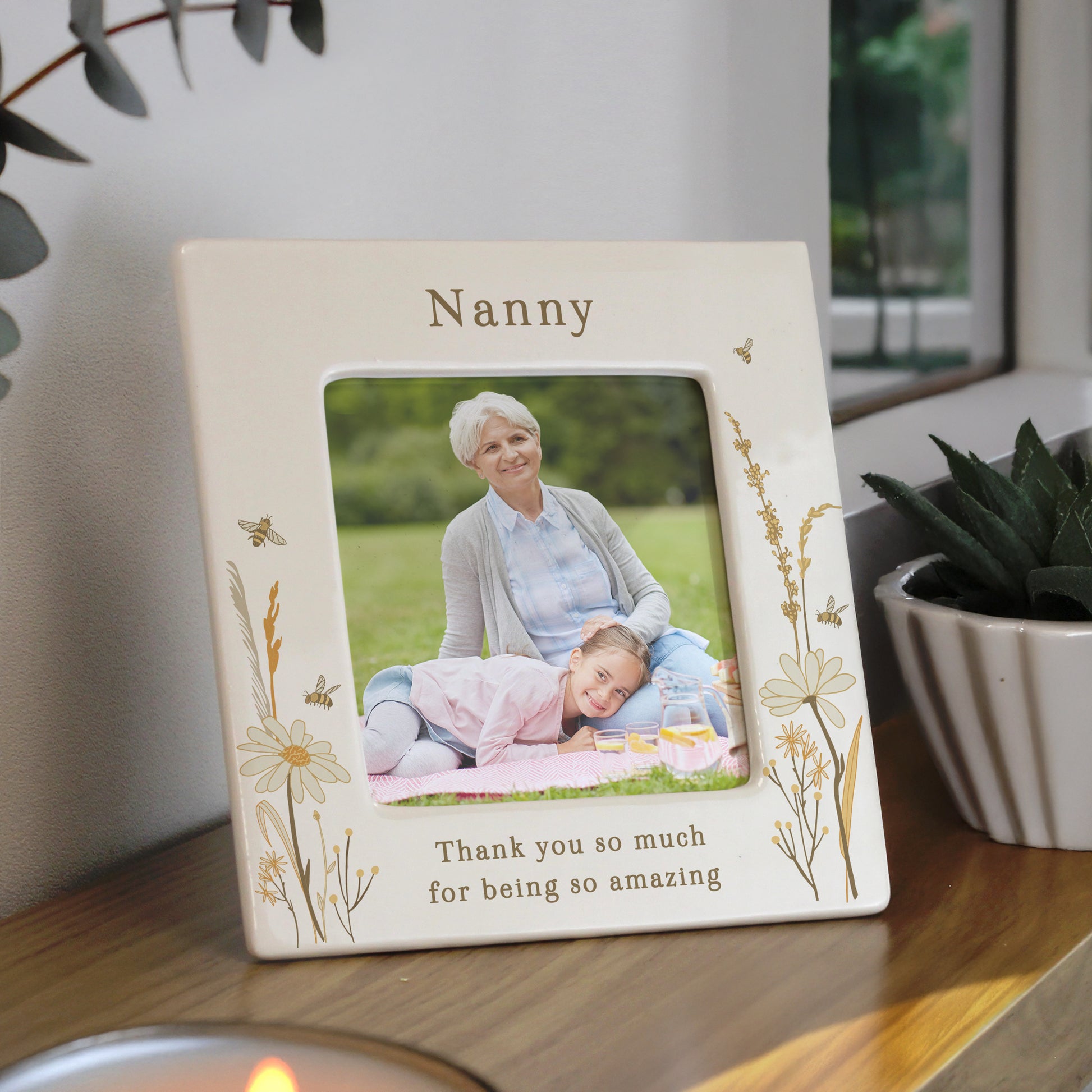 Personalised photo frame with a picture of a woman and a child, placed on a surface with plants in the background.
