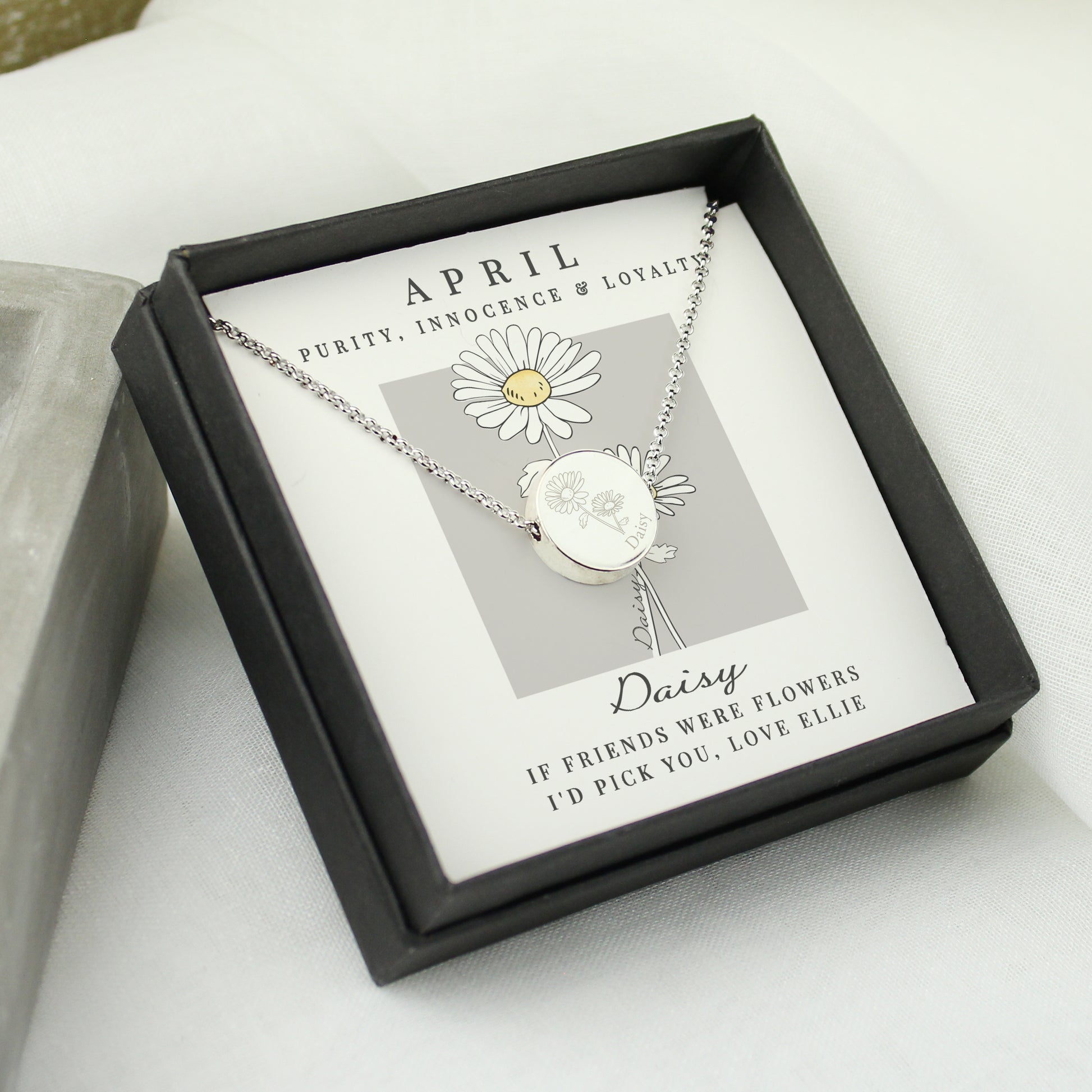 Silver coloured necklace with a daisy pendant in a black box on a white surface