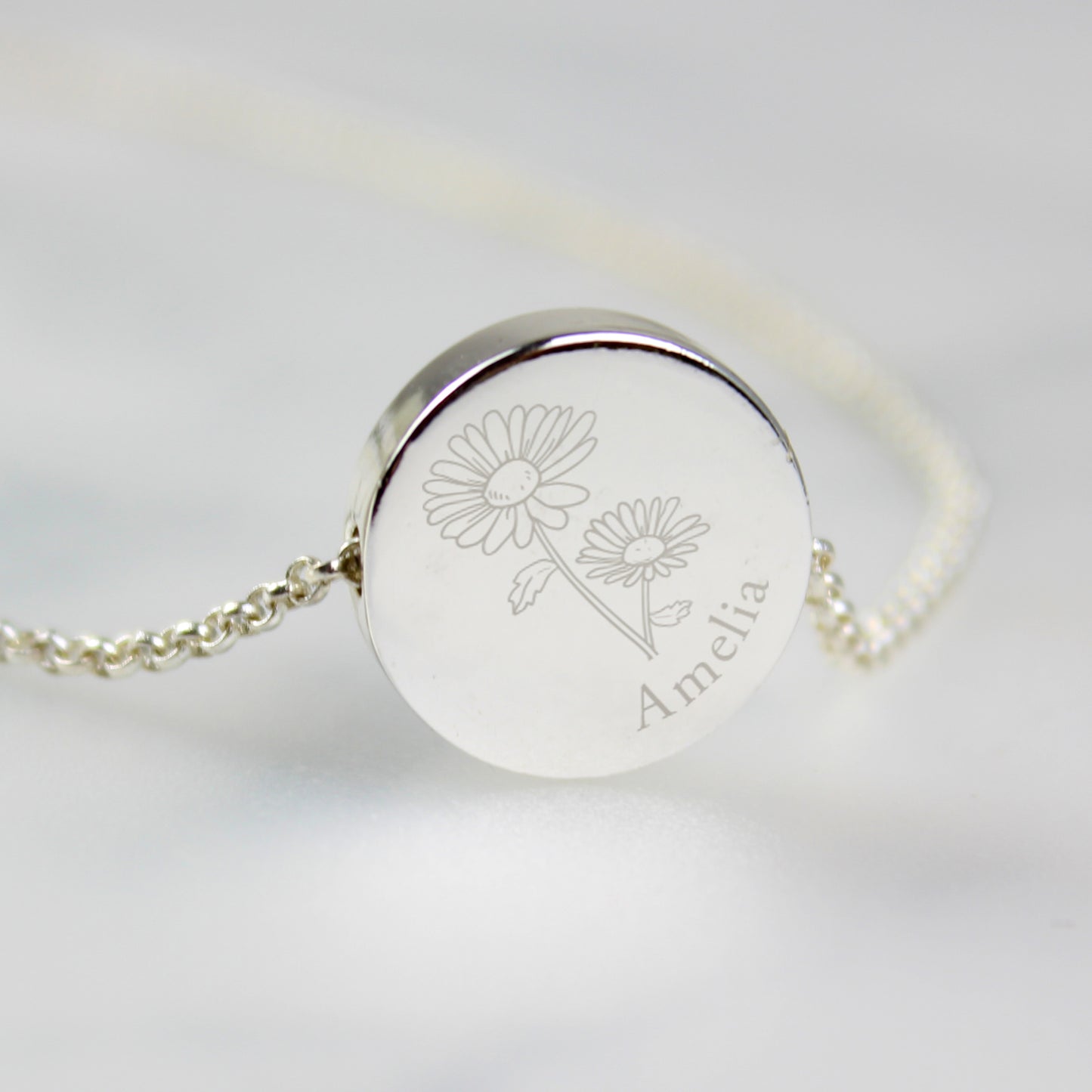 Silver coloured necklace with engraved floral design and name on a light grey background