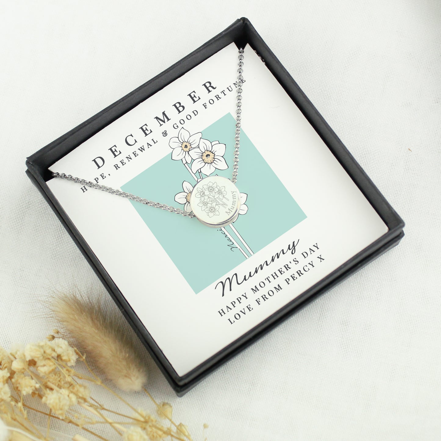 Silver necklace with a floral design in a gift box labeled 'December' on a light background.
