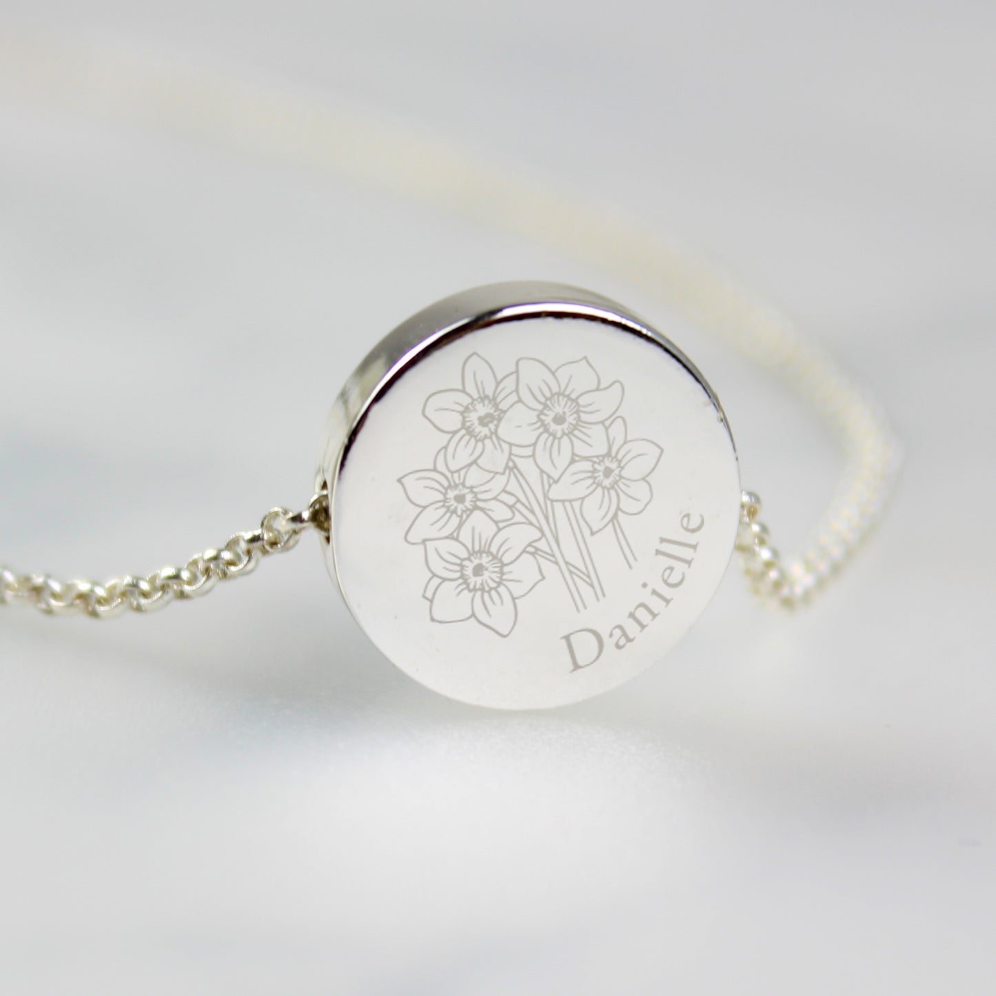 Silver coloured necklace with engraved floral design and name on a light grey background
