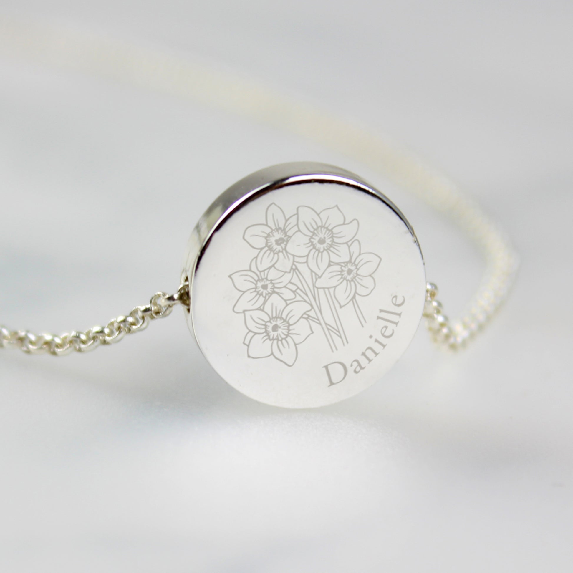 Silver coloured necklace with engraved floral design and name on a light grey background