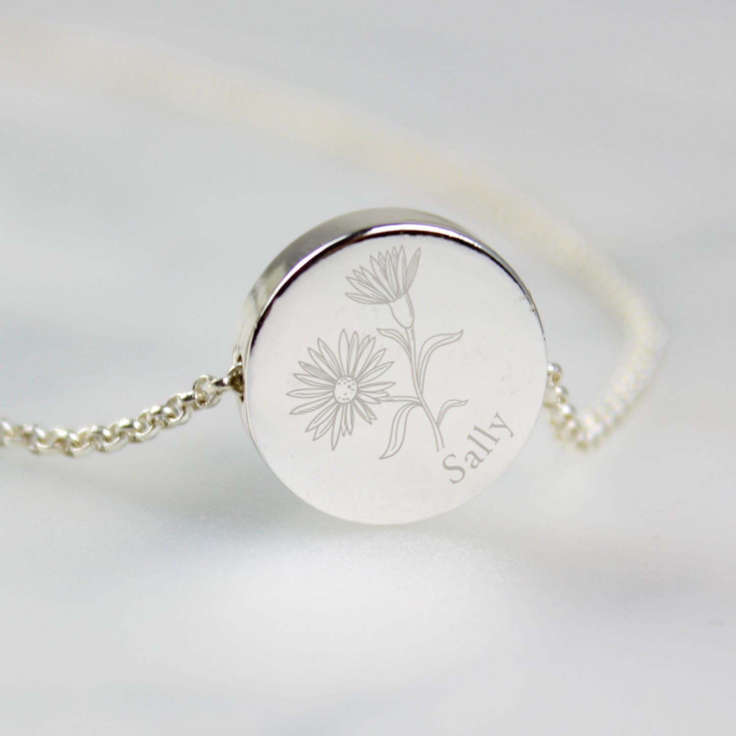 Silver coloured necklace with engraved floral design and name on a light grey background