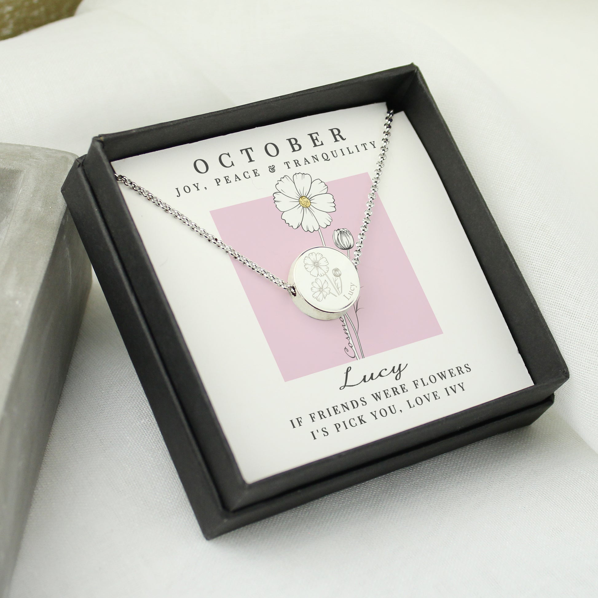 Silver coloured necklace with a daisy pendant in a black box on a white surface