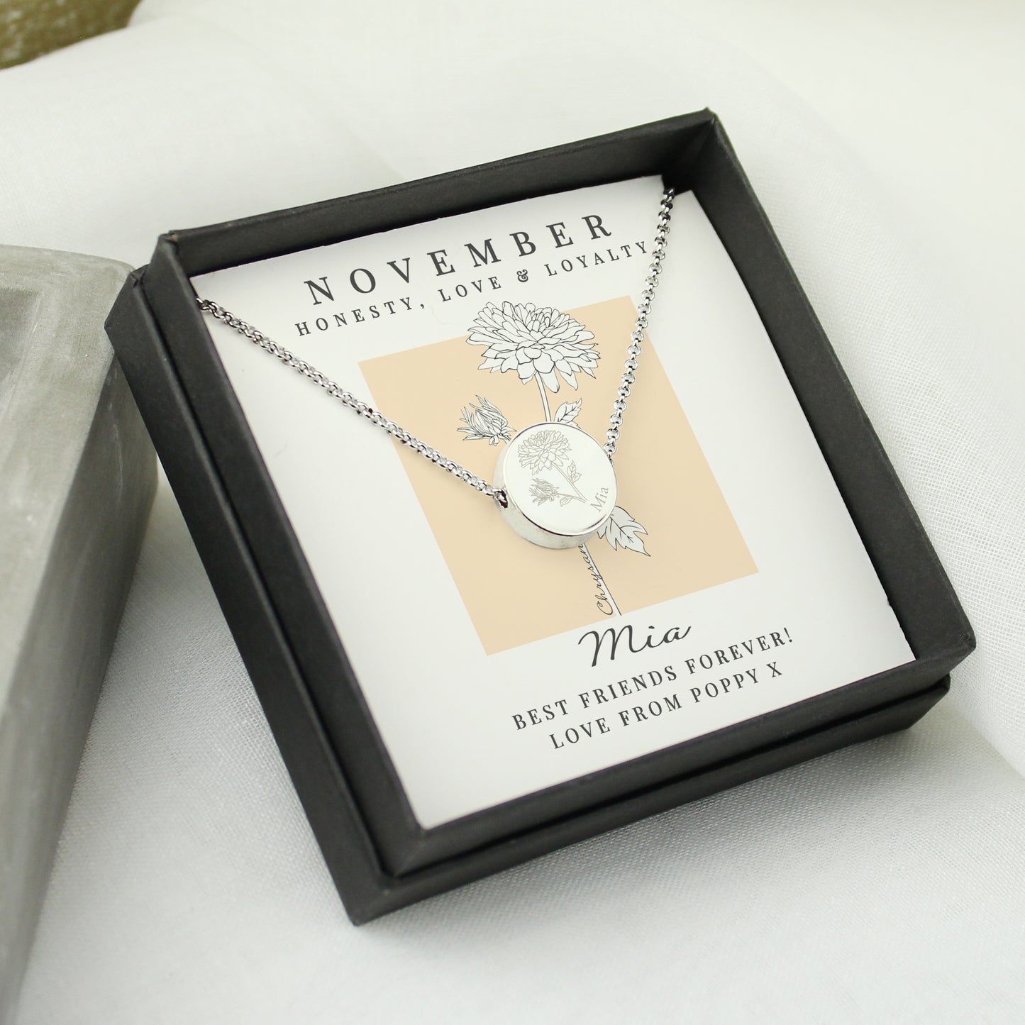 Silver necklace in a black box with a personalised message card on a light background