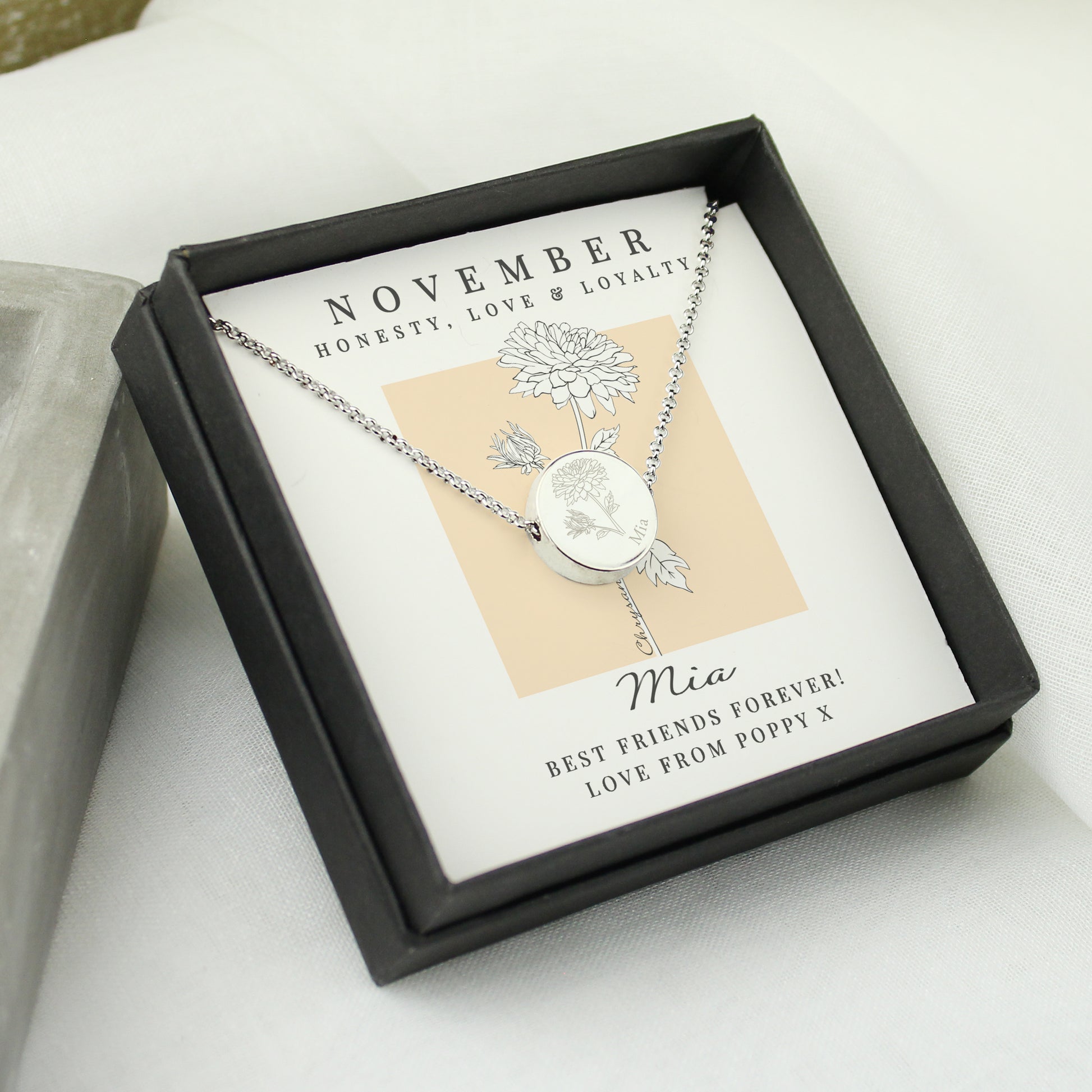 Silver necklace in a black box with a personalised message card on a light background