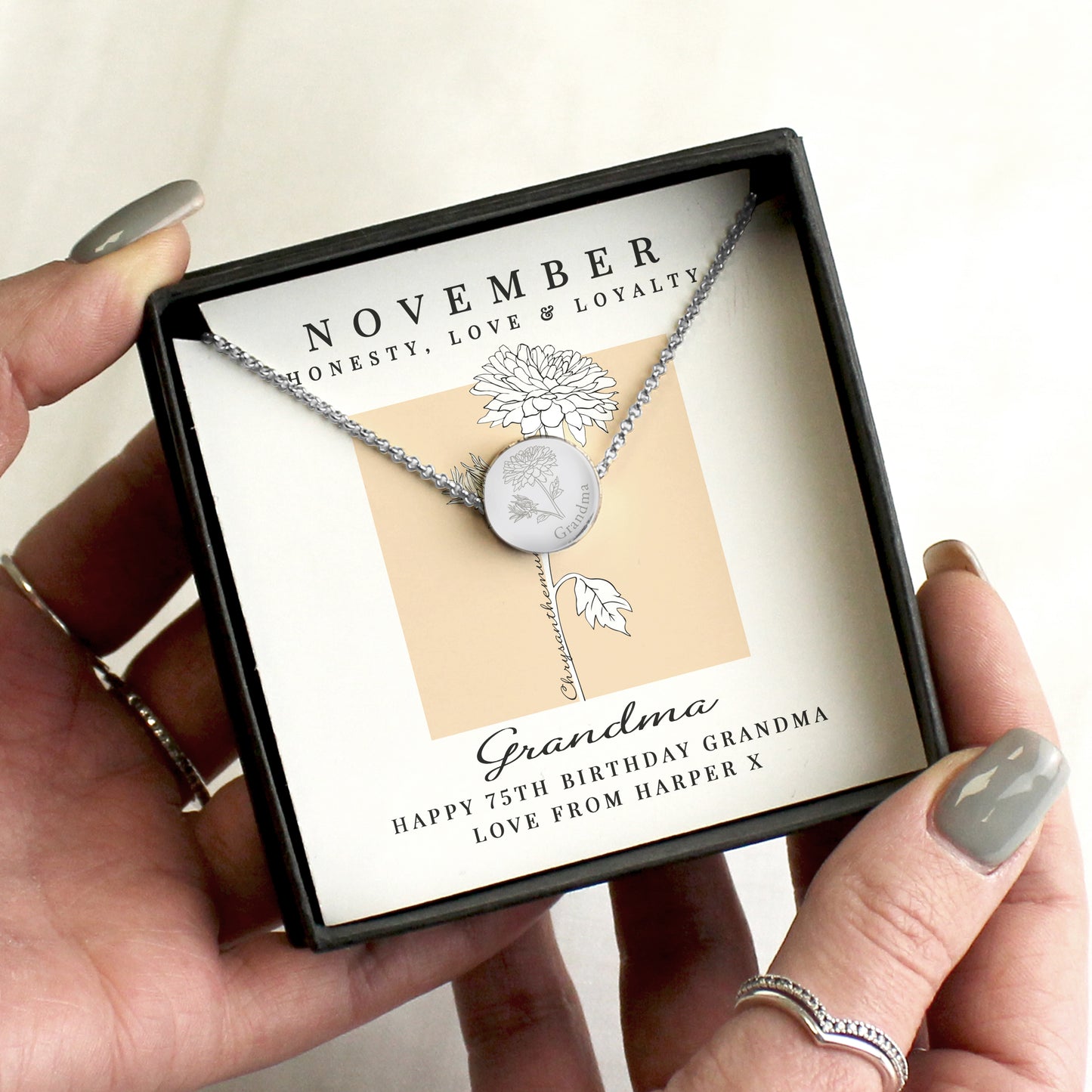 Silver necklace with a leaf design in a gift box, held by a hand.