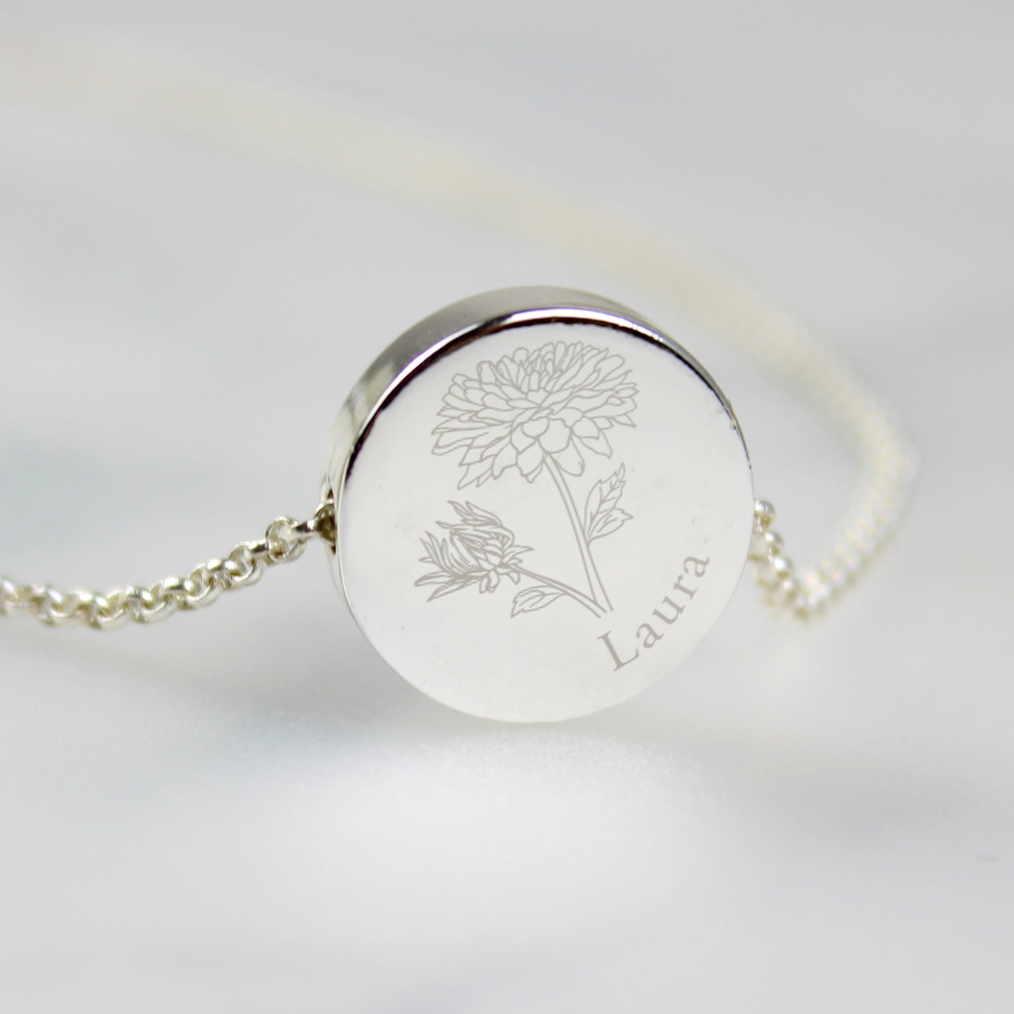 Silver coloured necklace with engraved floral design and name on a light grey background