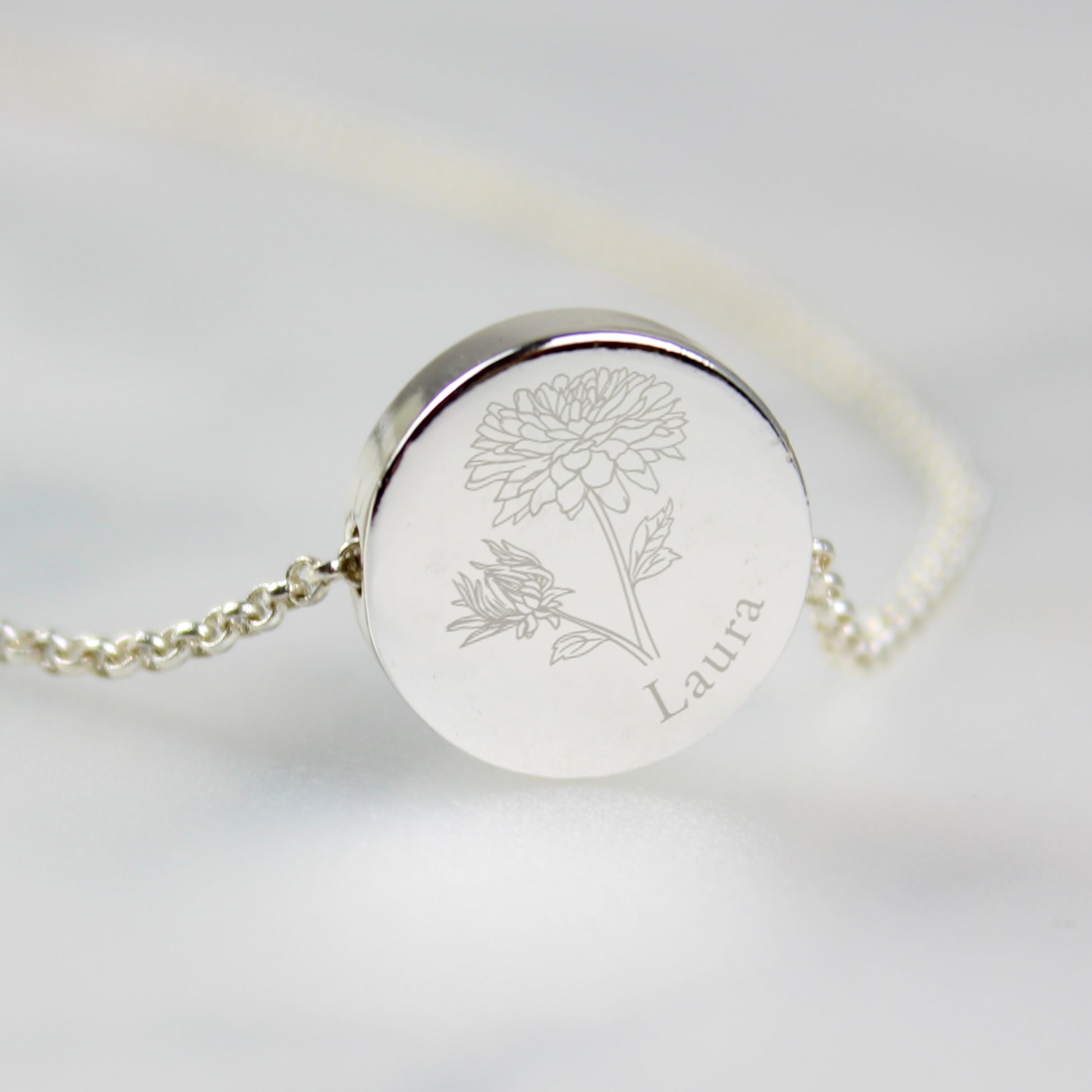 Silver coloured necklace with engraved floral design and name on a light grey background