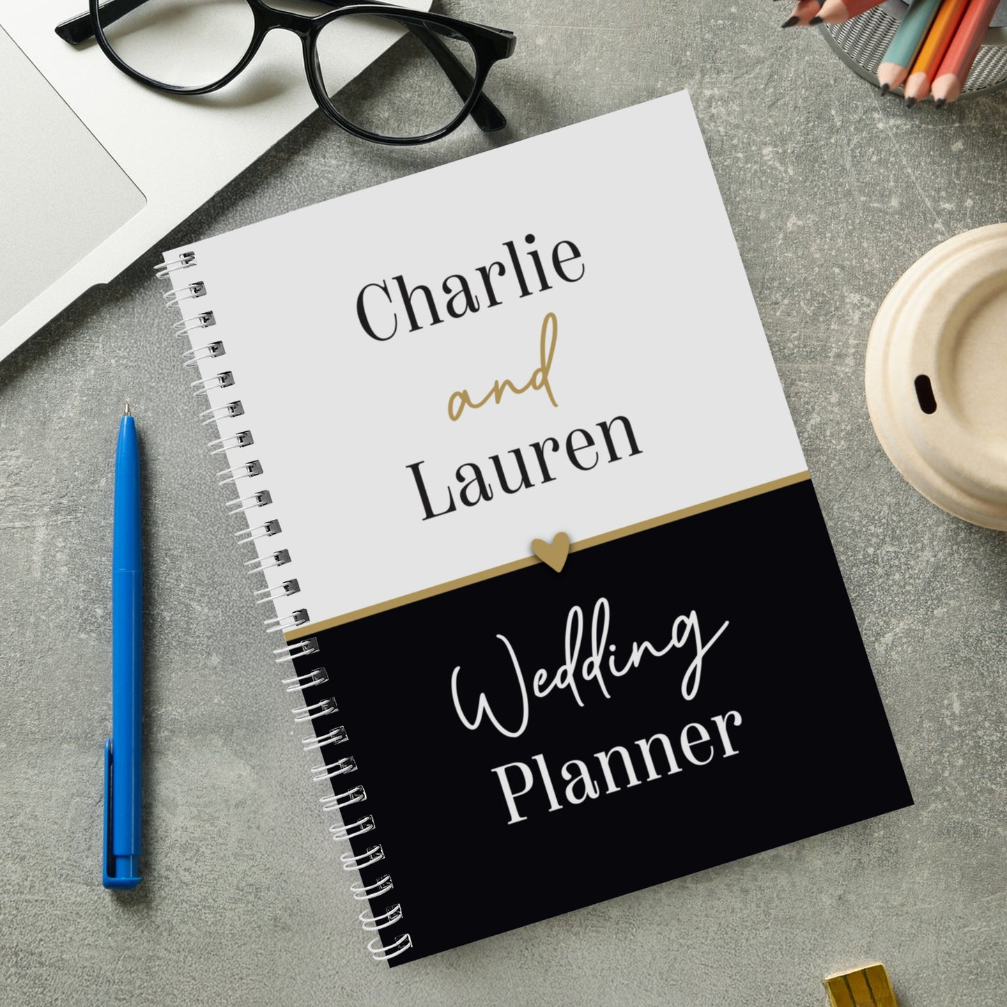Wedding planner notebook with 'Charlie and Lauren' on a grey surface with stationery items.