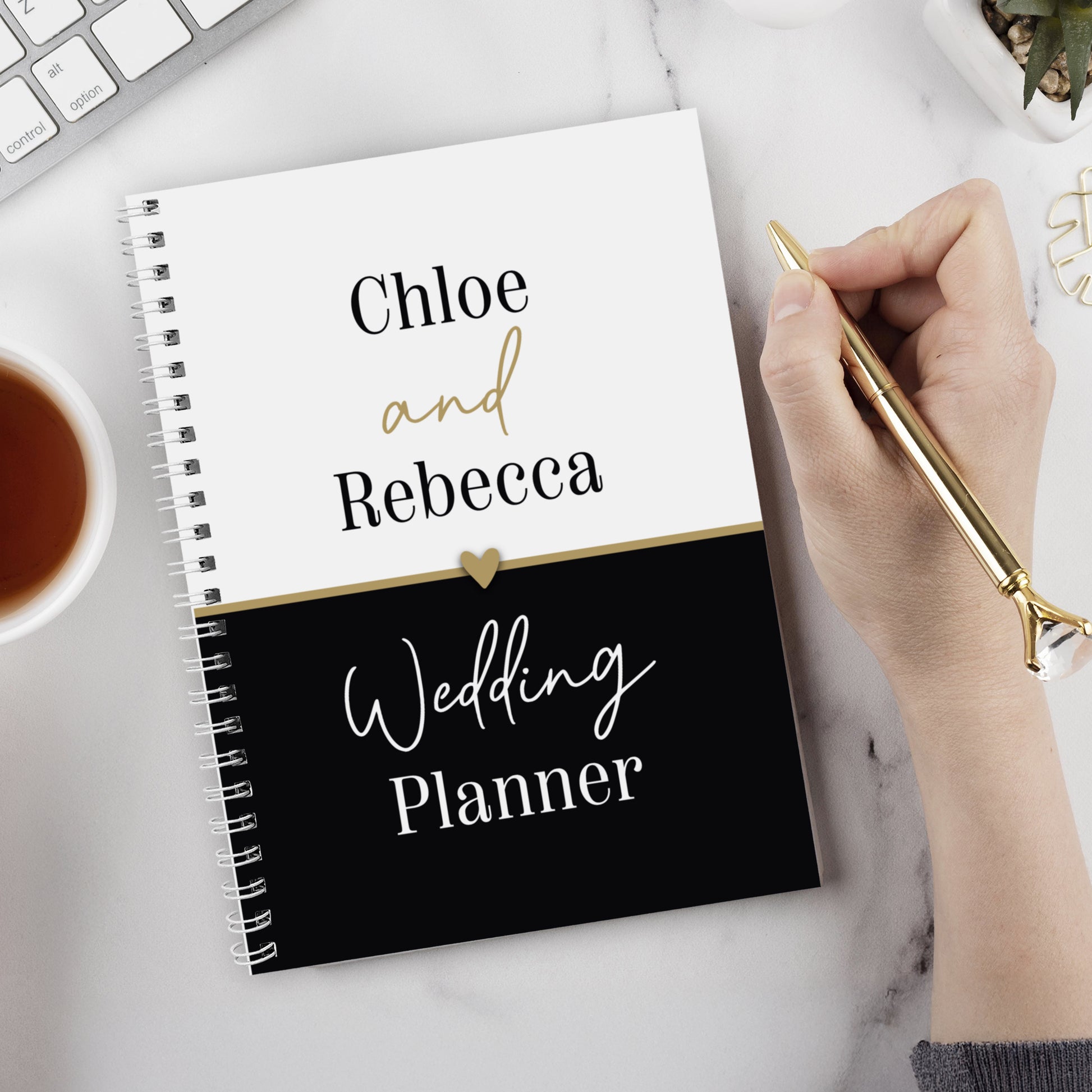 Wedding planner book titled 'Chloe and Rebecca Wedding Planner' on a desk with a hand holding a pen.