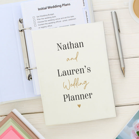 Wedding planner book titled 'Nathan and Lauren's Wedding Planner' on a wooden surface with a pen and other items.