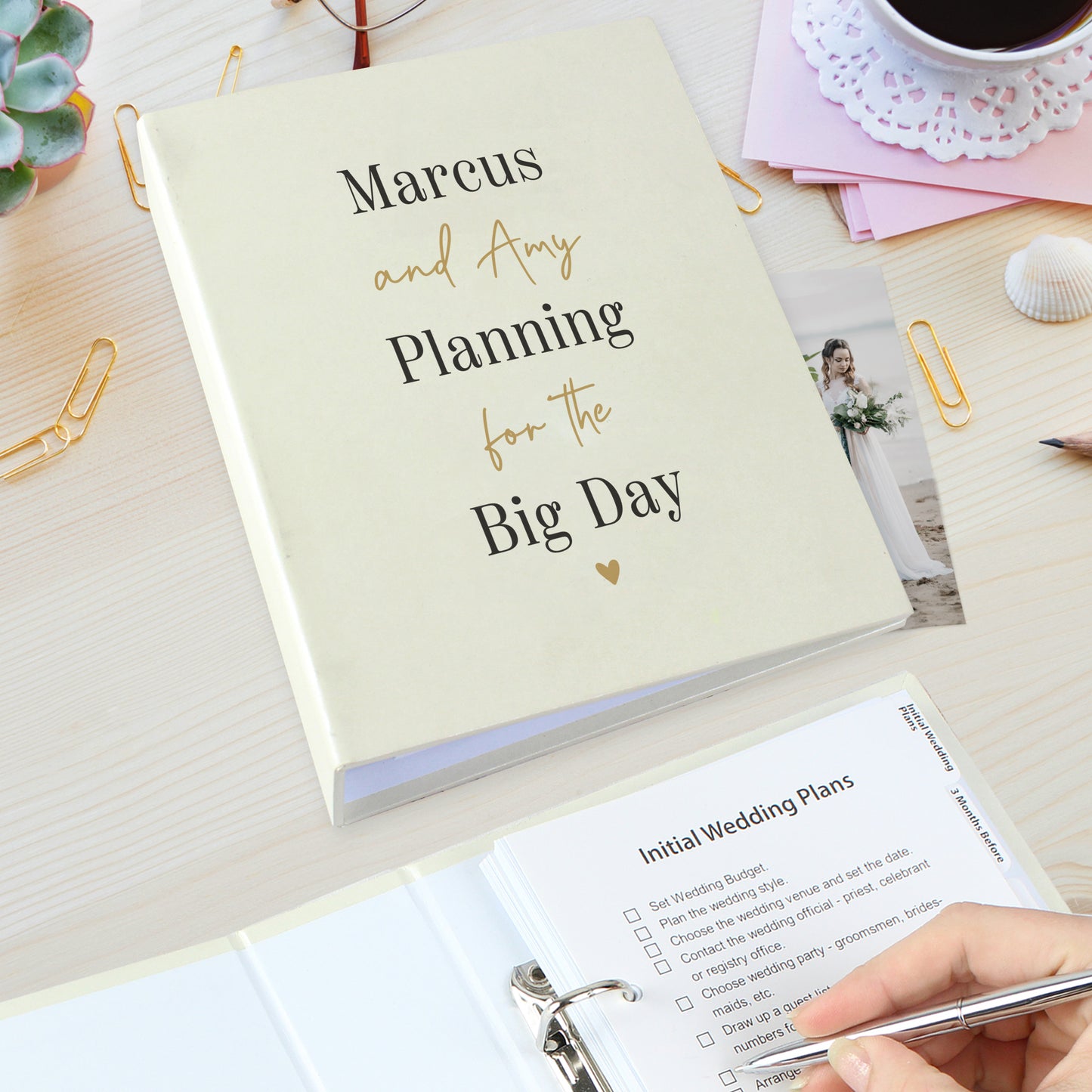 Wedding planning book titled 'Planning for the Big Day' with a hand holding a pen and a checklist on a desk.