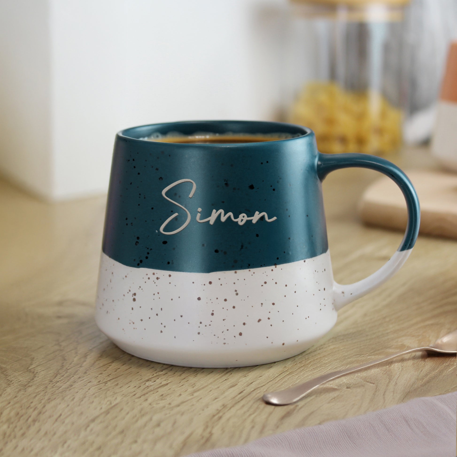 Personalised blue and white speckled mug with 'Simon' on a wooden surface