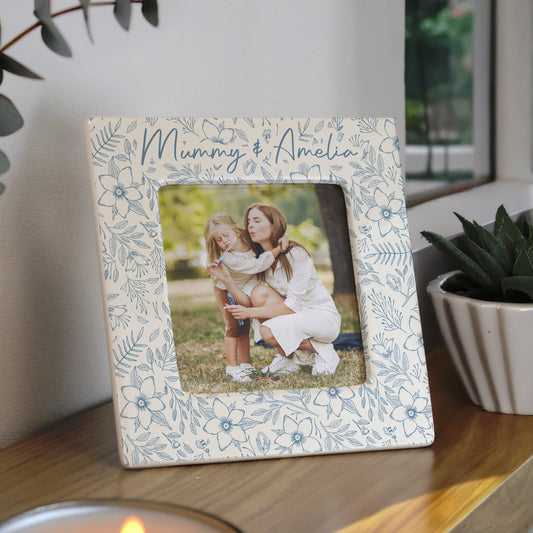 Floral photo frame with a picture of a woman and child on a wooden surface.