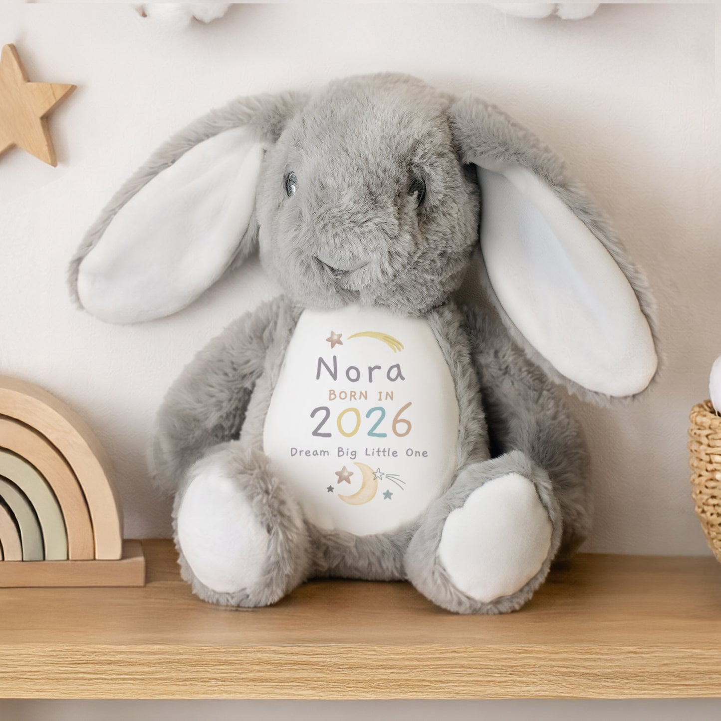 Grey and white soft toy bunny with personalised details - Norah Born in 2026 Dream Big Little One among moon and star images. Shown sat on a wooden shelf.