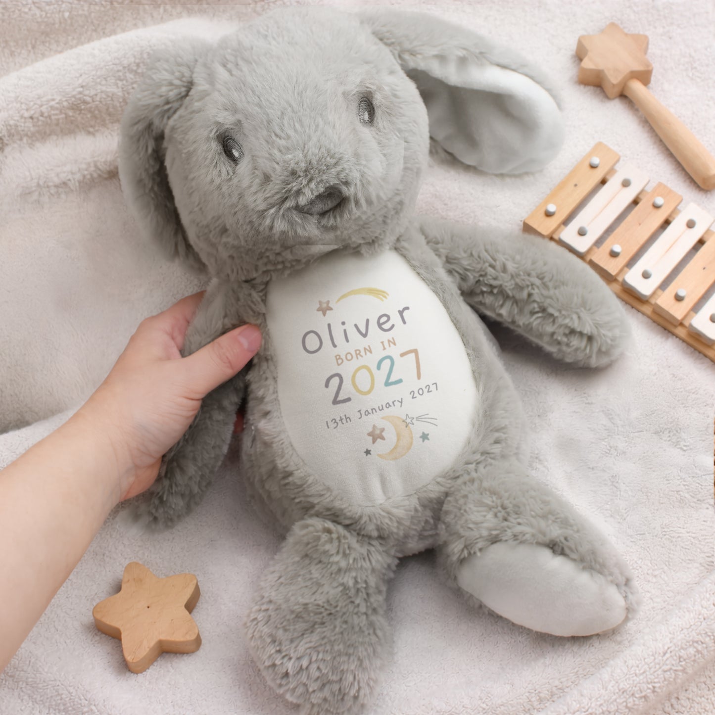 Grey and white soft toy bunny with personalised details - Oliver Born in 2027 13th January 2027 among moon and star images. Shown sat on a bed. among wooden toys.