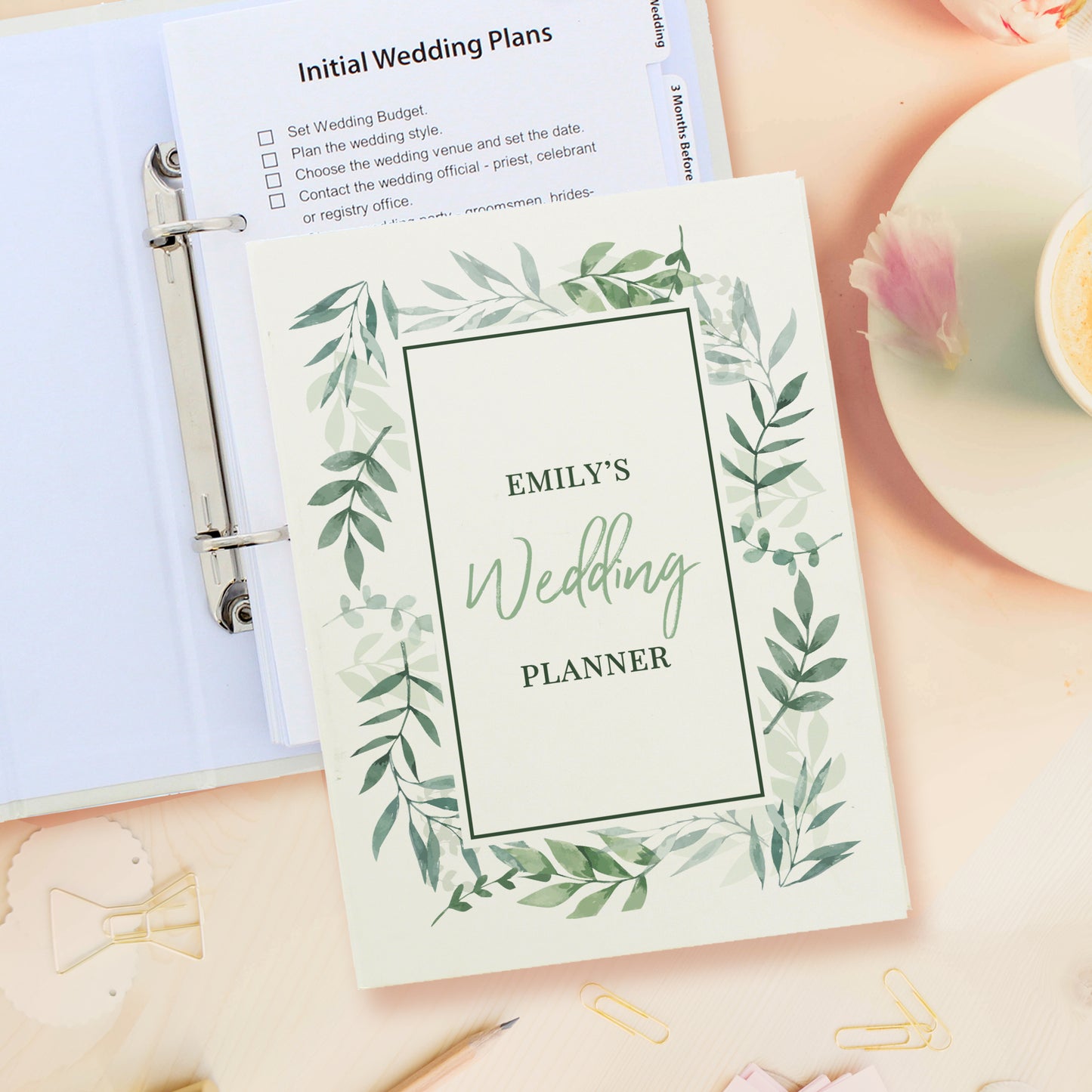 Wedding planner book with green leaf design on a desk with stationery items.