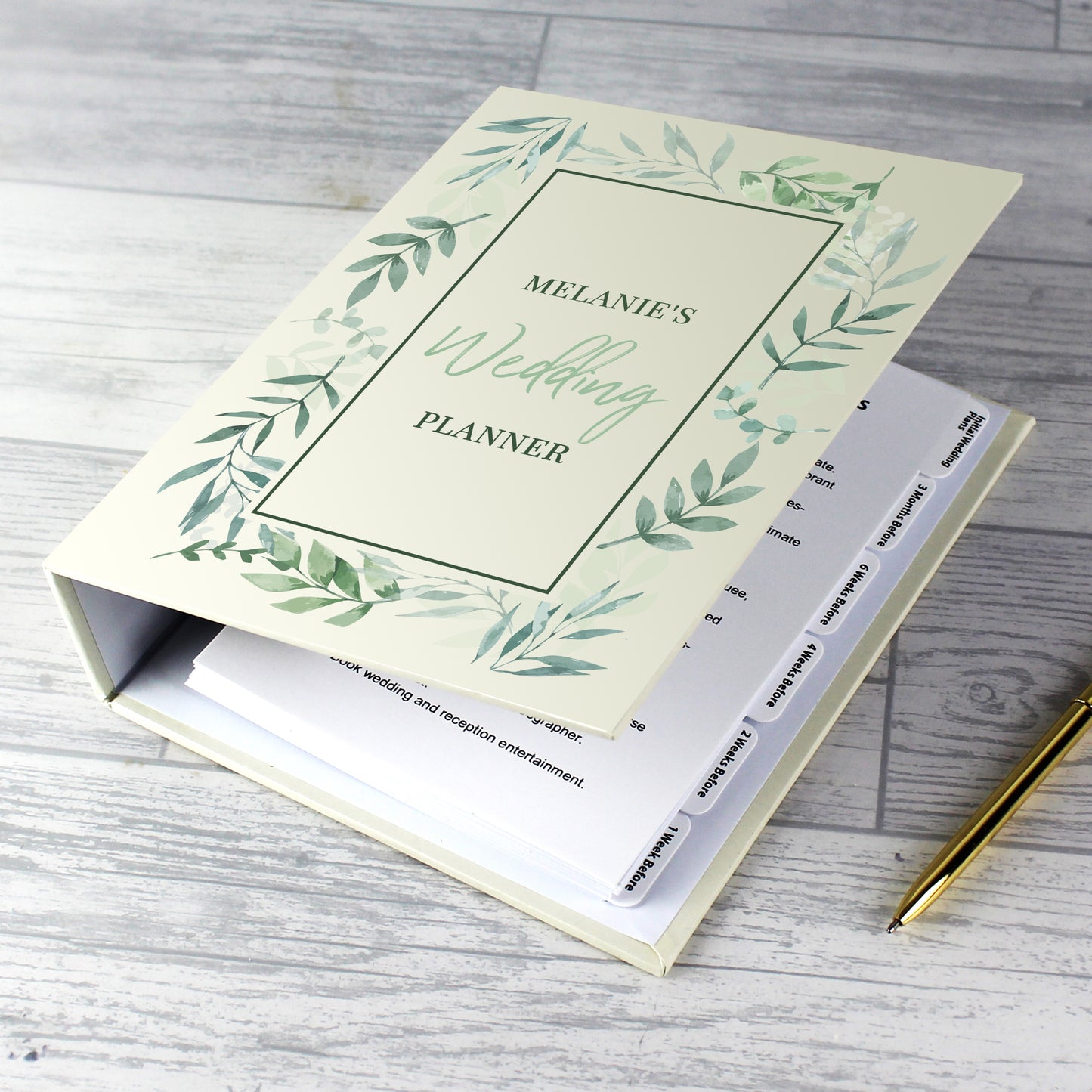 Wedding planner book with green leaf design on a wooden surface