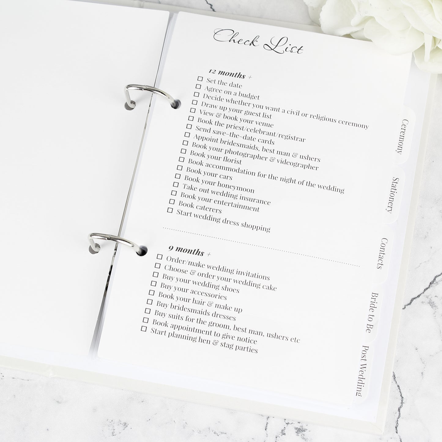 Wedding planning checklist on a marble surface with white flowers.