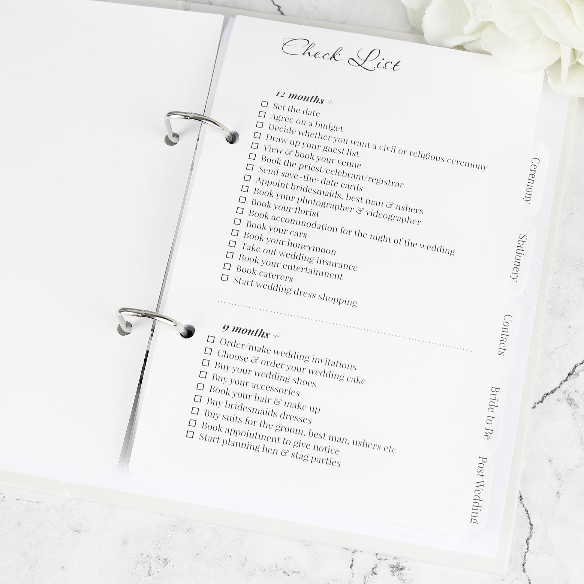 Wedding planning checklist on a marble surface with white flowers.