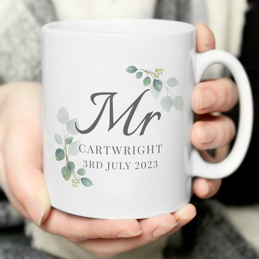 White mug with 'Mr Cartwright 3rd July 2023' text and decorative elements held by a person.