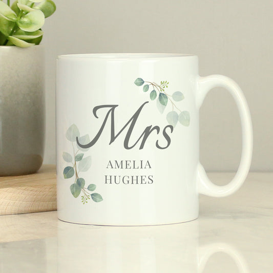 White mug with 'Mrs' and personalised name on a light surface with a plant in the background