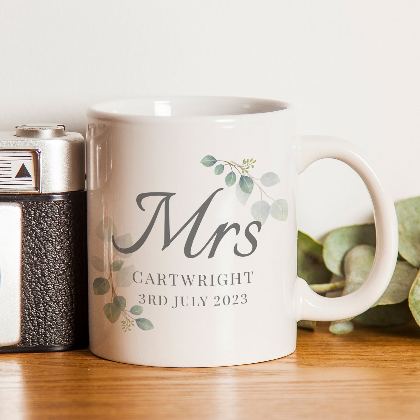 White mug with 'Mrs' and personalised text on a wooden surface with a plant in the background