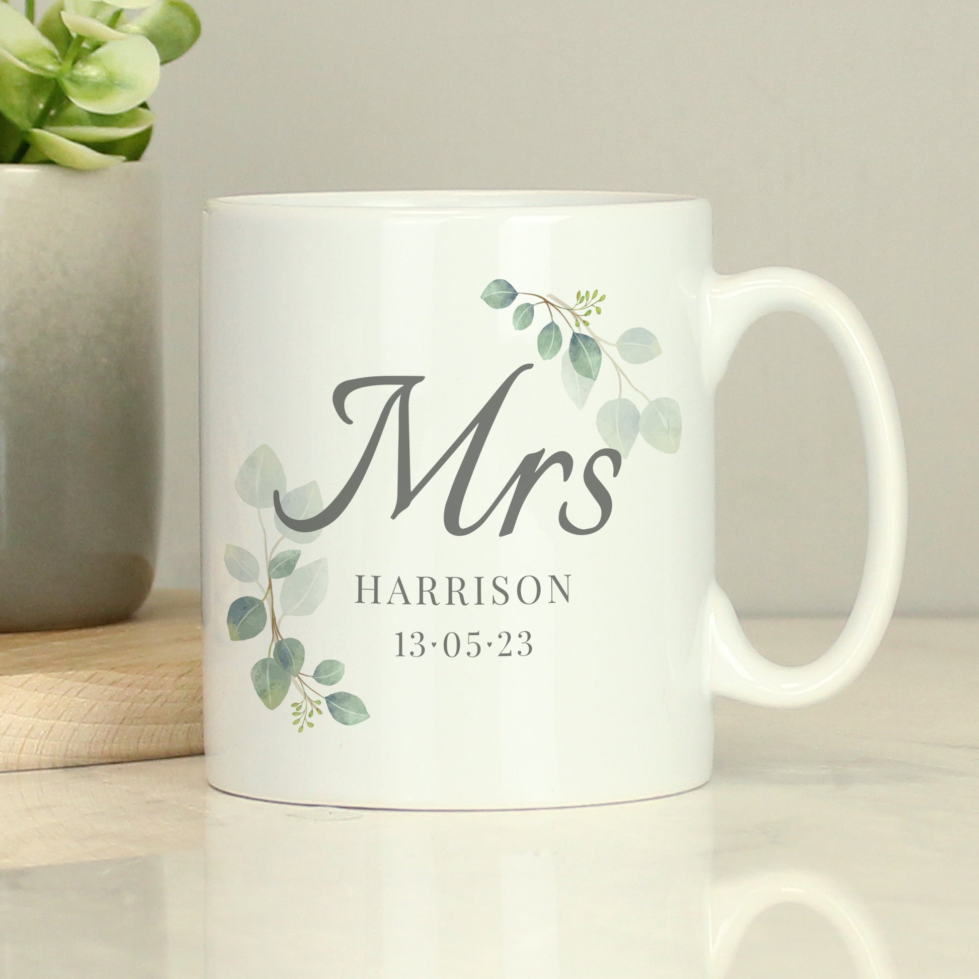 White mug with 'Mrs' and decorative elements on a light surface with a plant in the background